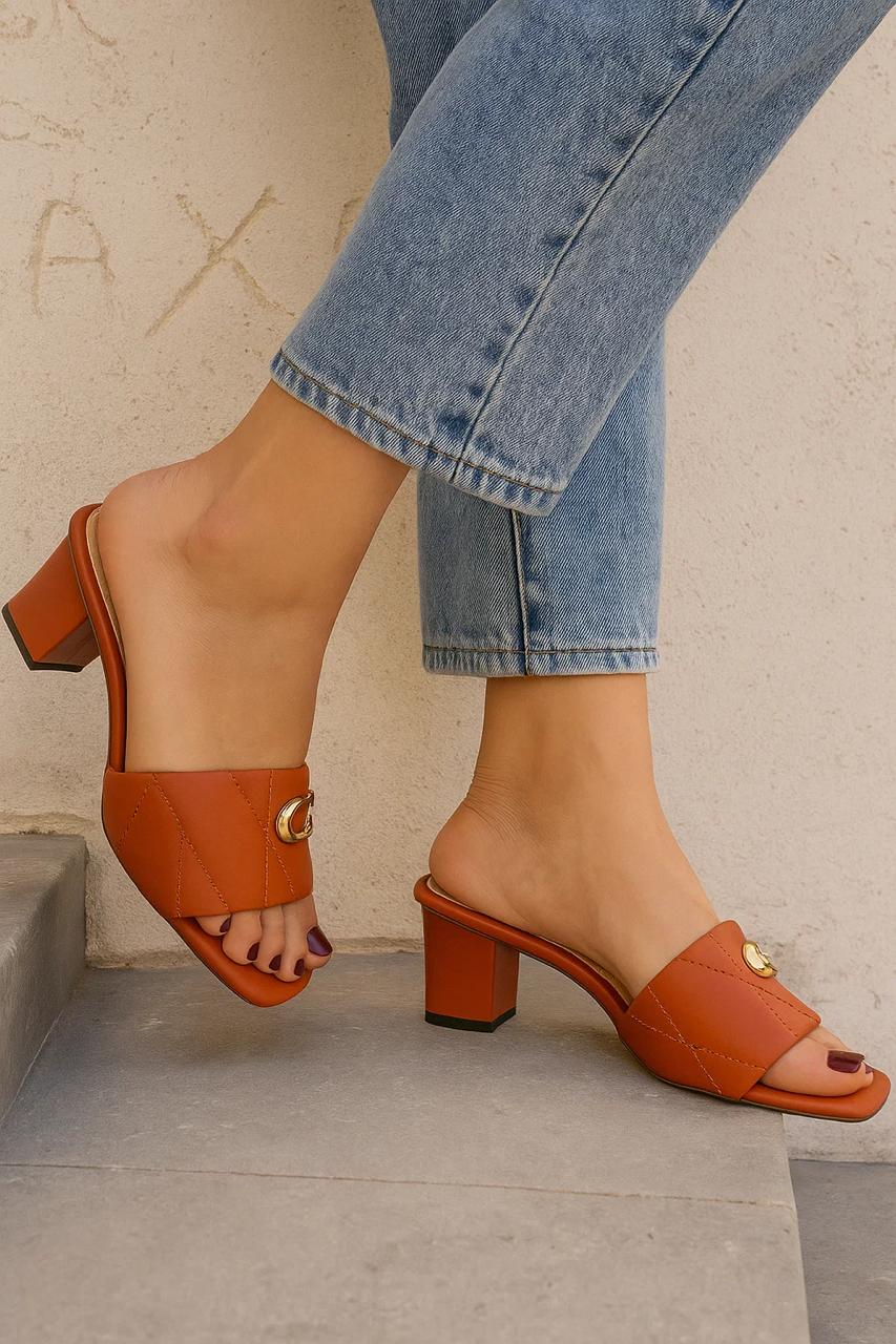 Brown sandals worn with blue jeans against a neutral background